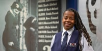 Keturah Johnson poses by a decades old, outdated poster with rules and uniforms for flight attendants,